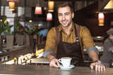 handsome young barista with cup of delicious coffee looking at camera