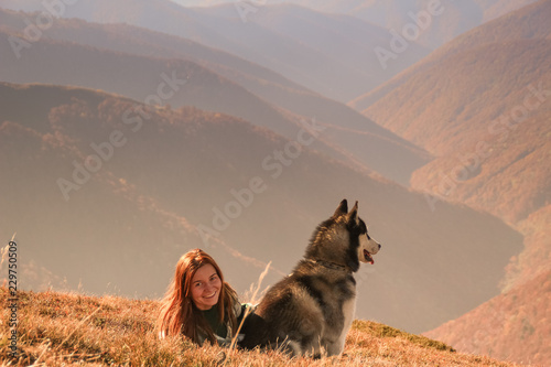 A girl in an authentic poncho with a green pattern play with husky. Ukrainian Carpathians in autumn time. Warm colored green leaves.Forests and mountains  top view. Travel with dog.