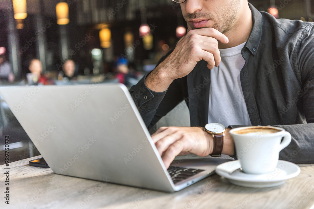 cropped shot of young freelancer working with laptop in cafe with cup of coffee on table