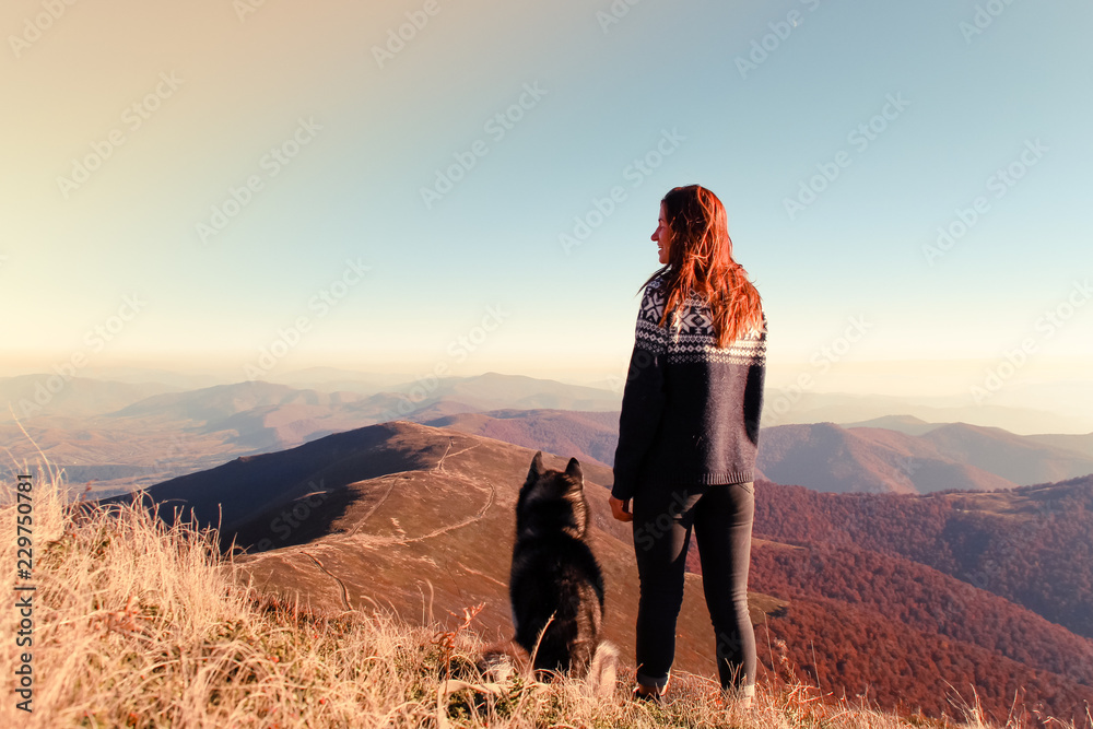 Red-hair girl in blue sweater with ornament play with husky. Ukrainian Carpathians in autumn time. Warm colored green leaves.Forests and mountains  top view. Travel with dog