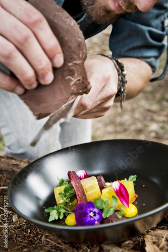 Chocolate being grated over a beet salad with edible flowers