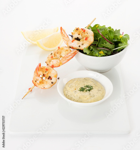 Grilled prawns on a skewer with chilly and pepper, bowl of mixed lettuce, Lemon wedges and tartare sauce with dill topping photo