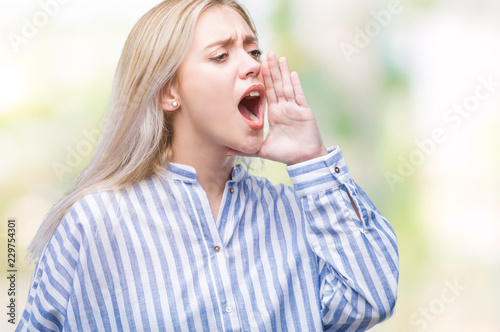 Young blonde woman over isolated background shouting and screaming loud to side with hand on mouth. Communication concept.
