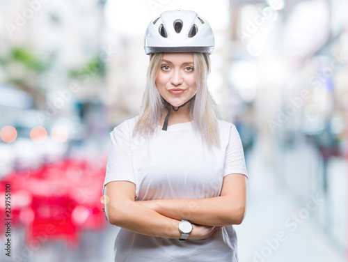 Young blonde woman wearing cyclist security helmet over isolated background happy face smiling with crossed arms looking at the camera. Positive person. © Krakenimages.com