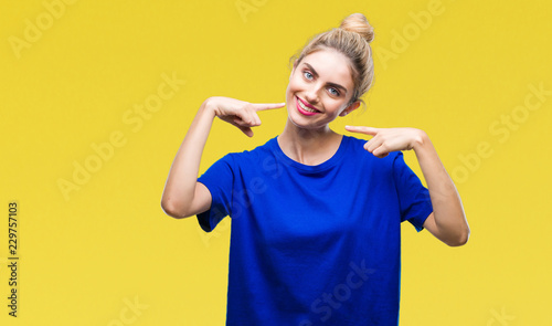 Young beautiful blonde and blue eyes woman wearing blue t-shirt over isolated background smiling confident showing and pointing with fingers teeth and mouth. Health concept.