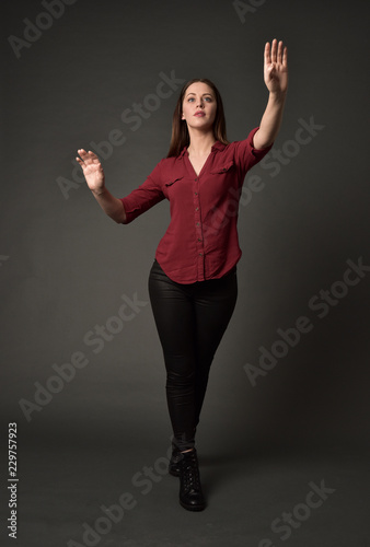 full length portrait of brunette girl wearing  red shirt and leather pants. standing pose, on grey studio background. © faestock