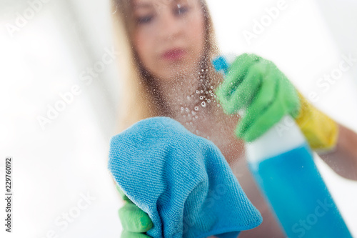 Beautiful young woman is using a duster and a spray to cleaning windows at home. photo
