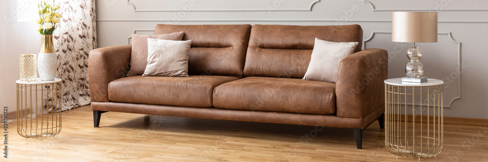 Panoramic view of brown leather sofa between two stylish tables with marble tops, real photo - obrazy, fototapety, plakaty 