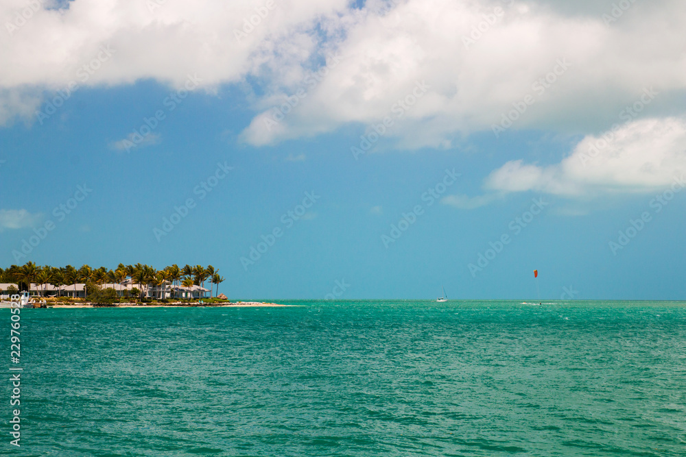 Turquoise blue sea horizon and island with sandy beach, palm trees and beachfront house cottages, Sunset Key in the Key West, Florida USA