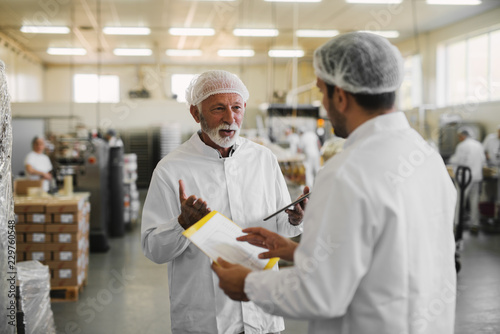 Two serious business man in sterile clothes standing in food factory and talking about business.