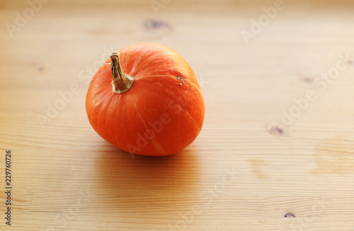 One little orange pumpkin on light wooden background