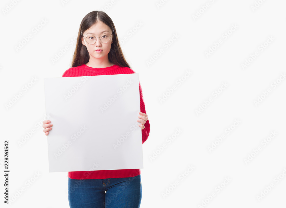 Young Chinese woman over isolated background holding blank banner with a confident expression on smart face thinking serious Young Chinese woman over isolated background holding blank banner with a confident expression on smart face thinking serious