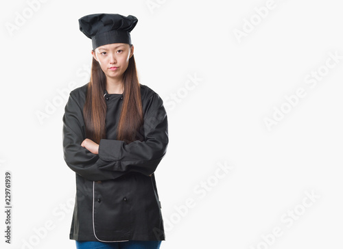 Young Chinese woman over isolated background wearing chef uniform skeptic and nervous, disapproving expression on face with crossed arms. Negative person.