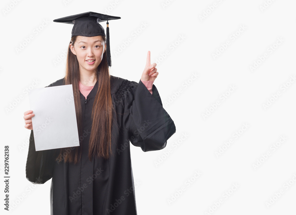 Young Chinese woman wearing graduate uniform holding paper degree surprised with an idea or question pointing finger with happy face, number one Young Chinese woman wearing graduate uniform holding paper degree surprised with an idea or question pointing finger with happy face, number one