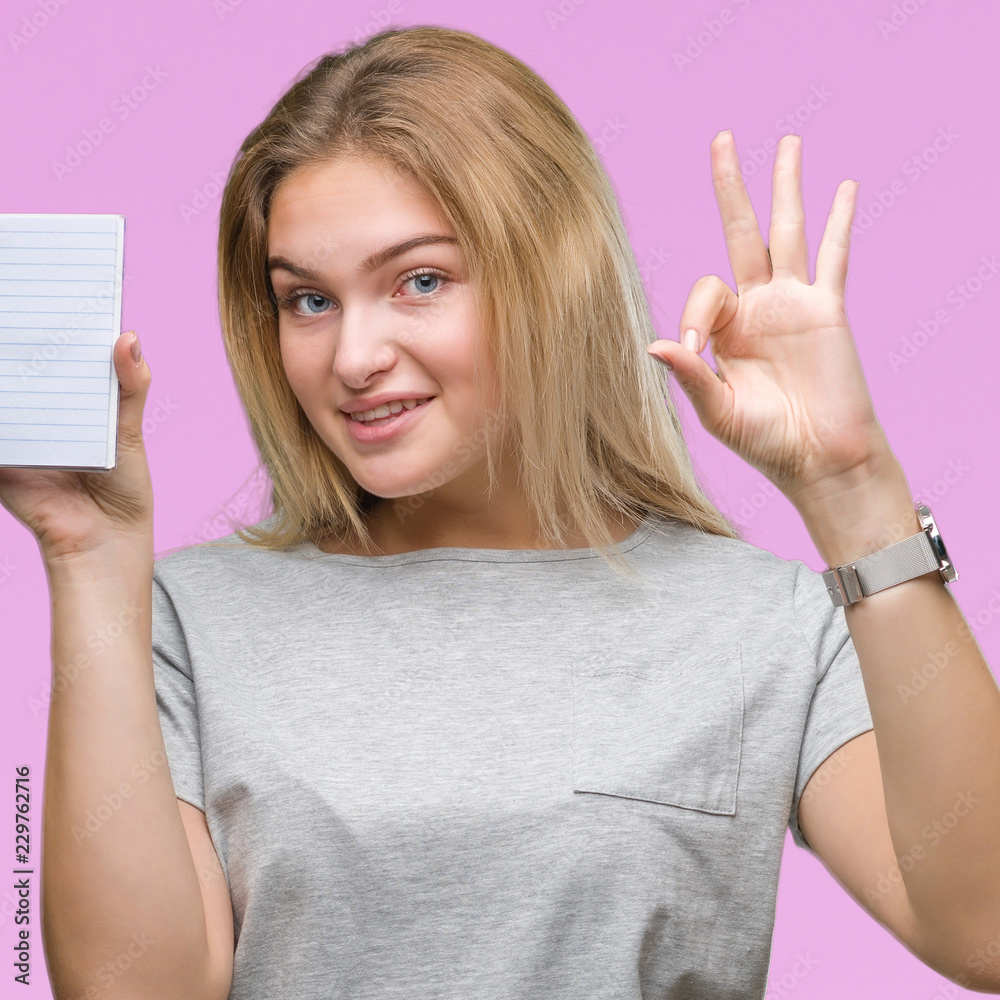 Obraz premium Young caucasian woman holding blank notebook over isolated background doing ok sign with fingers, excellent symbol