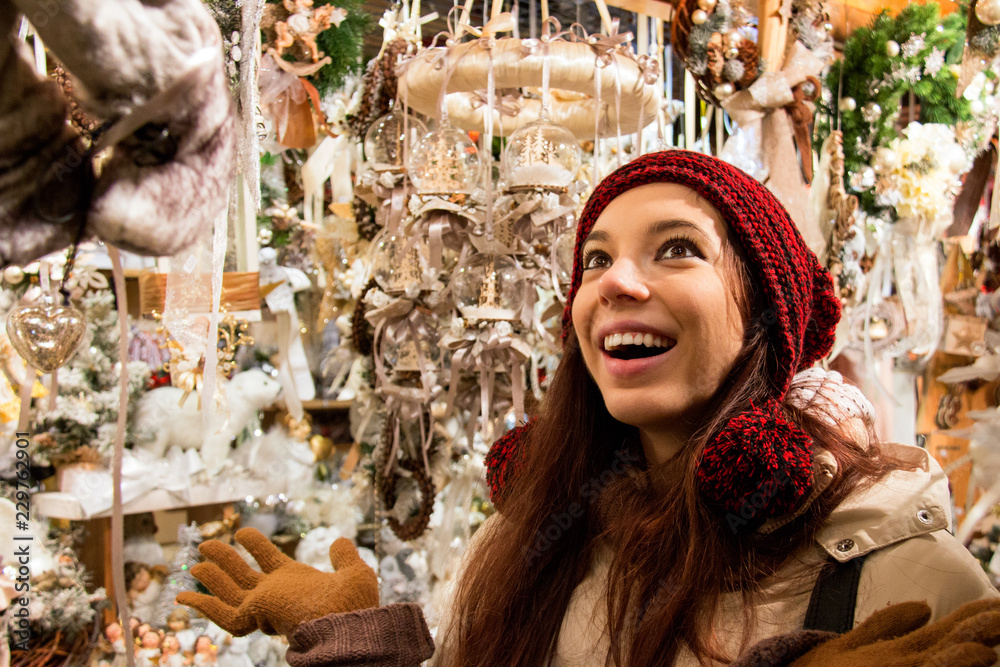 Smiling happy woman in front of display window shopping Christmas tree decorations, balls and other seasonal crafted products for Christmas Holidays, Girl is surprised of wide variety of styles