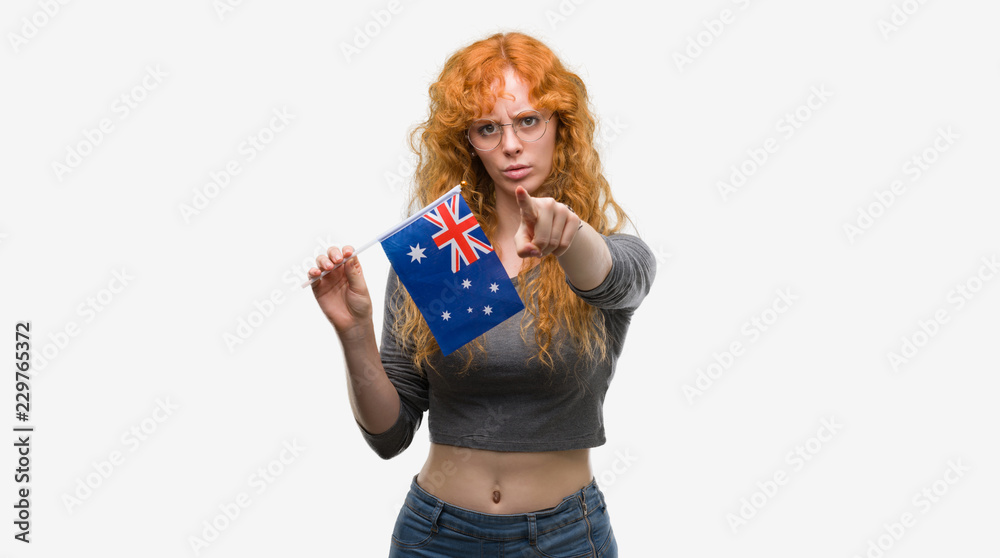 Young redhead woman holding flag of Australia pointing with finger to the camera and to you, hand sign, positive and confident gesture from the front Young redhead woman holding flag of Australia pointing with finger to the camera and to you, hand sign, positive and confident gesture from the front
