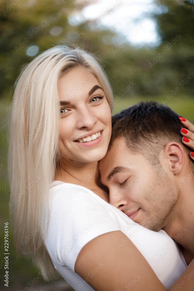 Loving couple standing on grass in nature green park with beautiful sundown light hugging. Man lies on woman's breast. Loving couple standing on grass in nature green park with beautiful sundown light hugging. Man lies on woman's breast.