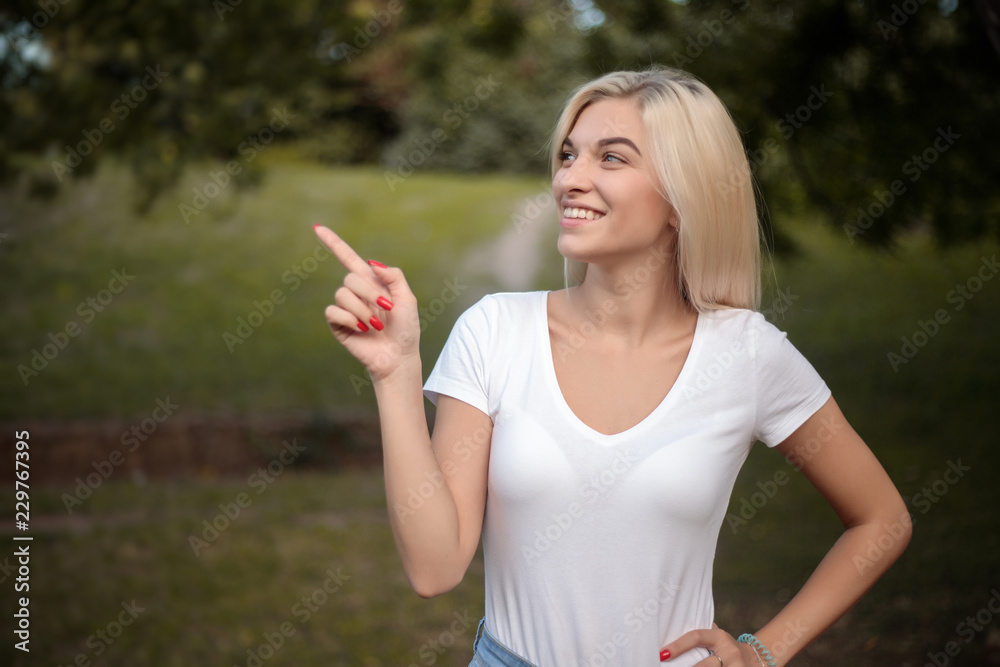 Happy beautiful young cute woman standing on grass in nature green park with beautiful sundown light looking aside showing copyspace pointing. Happy beautiful young cute woman standing on grass in nature green park with beautiful sundown light looking aside showing copyspace pointing.