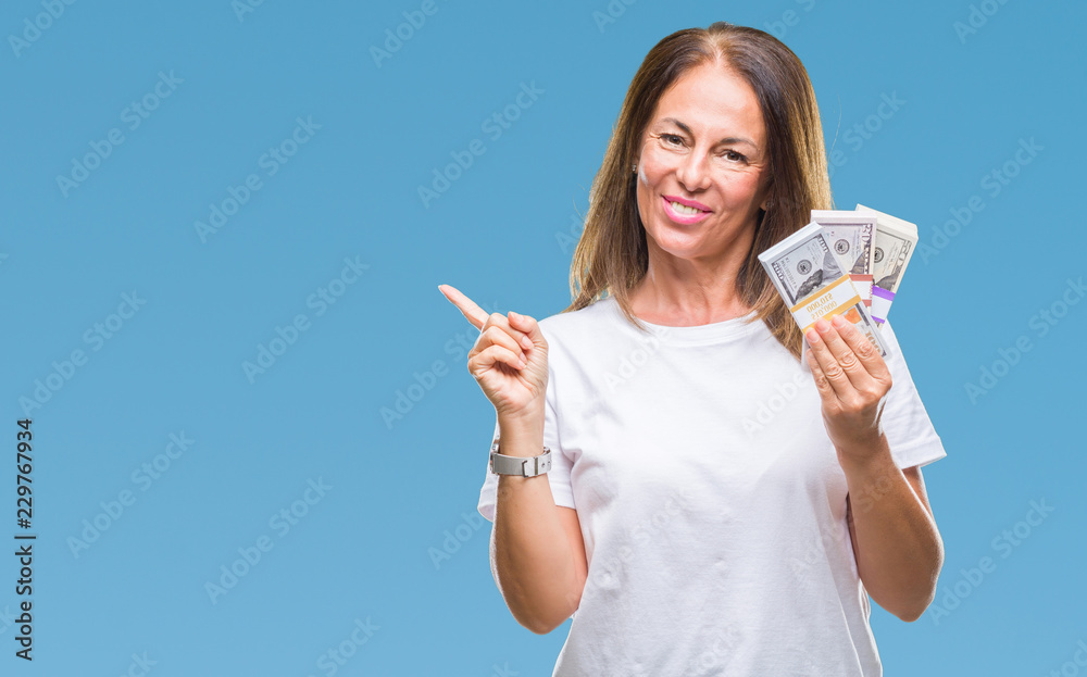 Middle age hispanic woman holding bunch of dollars over isolated background very happy pointing with hand and finger to the side Middle age hispanic woman holding bunch of dollars over isolated background very happy pointing with hand and finger to the side