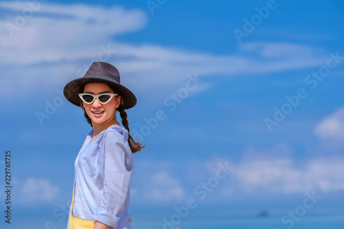 portrait beautiful woman in outdoor the beach with posing relax smile happy in holiday by wear hat and sunglasses fashion sunglasses and bag yellow with blue sky background