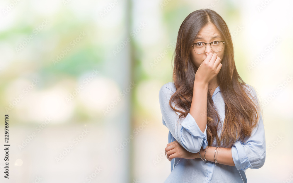 Young asian business woman wearing glasses over isolated background smelling something stinky and disgusting, intolerable smell, holding breath with fingers on nose. Bad smells concept. Young asian business woman wearing glasses over isolated background smelling something stinky and disgusting, intolerable smell, holding breath with fingers on nose. Bad smells concept.