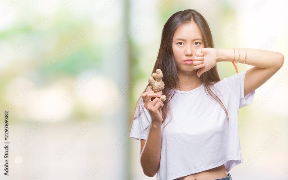 Young asian woman holding fresh organic over isolated background with angry face, negative sign showing dislike with thumbs down, rejection concept Young asian woman holding fresh organic over isolated background with angry face, negative sign showing dislike with thumbs down, rejection concept