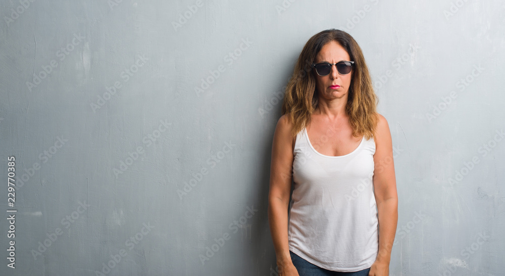 Middle age hispanic woman over grey wall wearing sunglasses skeptic and nervous, frowning upset because of problem. Negative person. Middle age hispanic woman over grey wall wearing sunglasses skeptic and nervous, frowning upset because of problem. Negative person.