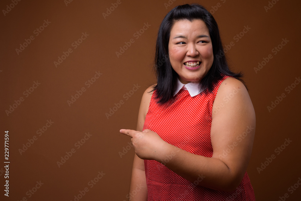 Obraz premium Beautiful overweight woman laughing and pointing finger to copy space