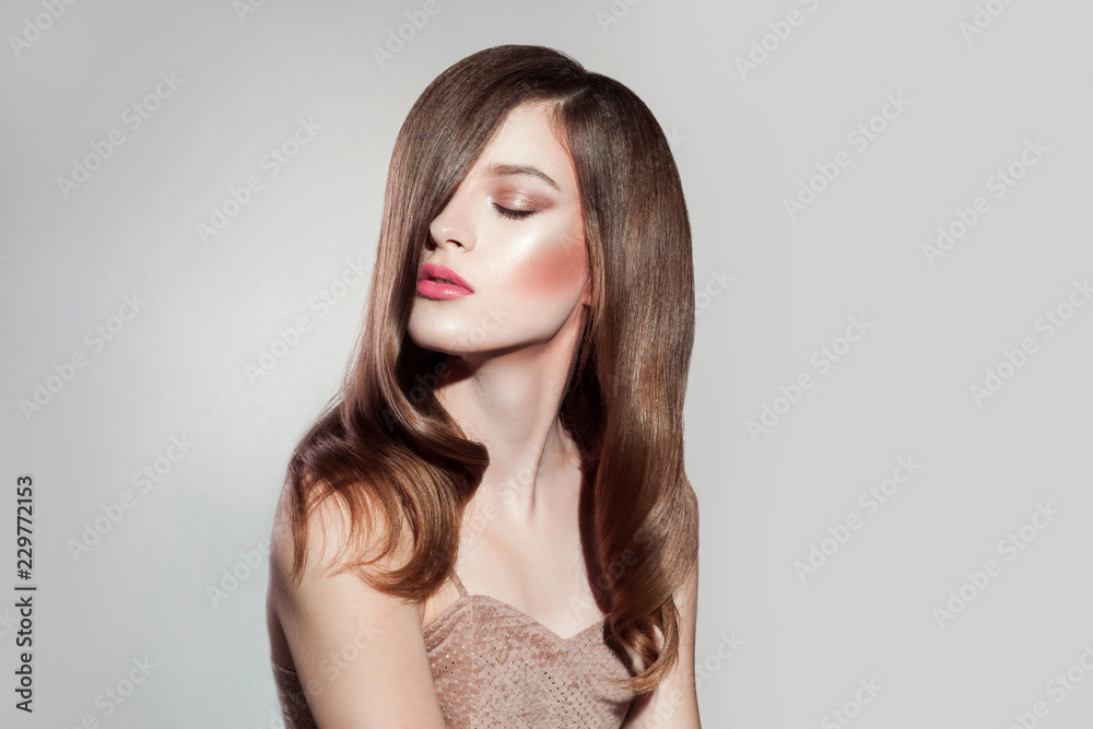 Naklejka premium portrait of attractive brunette woman with makeup and straight shiny hairs, closed eyes posing on isolated grey background. indoor, studio shot on copy space.