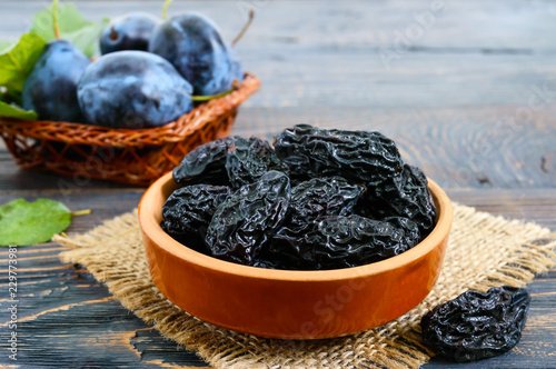 Prunes in a clay bowl and fresh plums, leaves on a wooden table. Fresh prunes for healthy life.