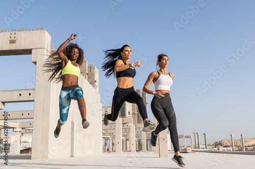 Obraz na płótnie Three beautiful Caucasian and African American fitness female athletes exercising in a concrete open stadium on a hot Summer day wearing bright sports wear w salonie
