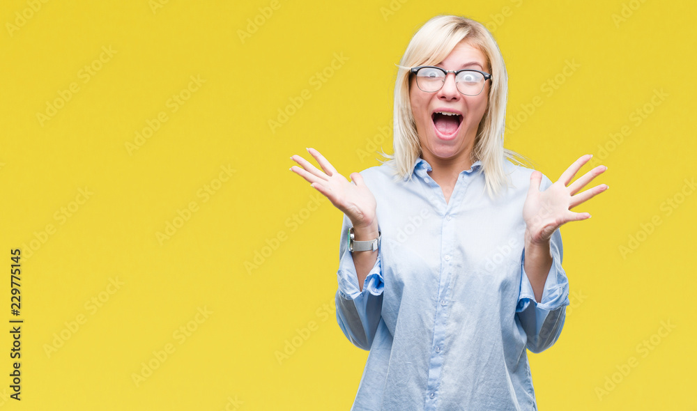 Young beautiful blonde business woman wearing glasses over isolated background celebrating crazy and amazed for success with arms raised and open eyes screaming excited. Winner concept