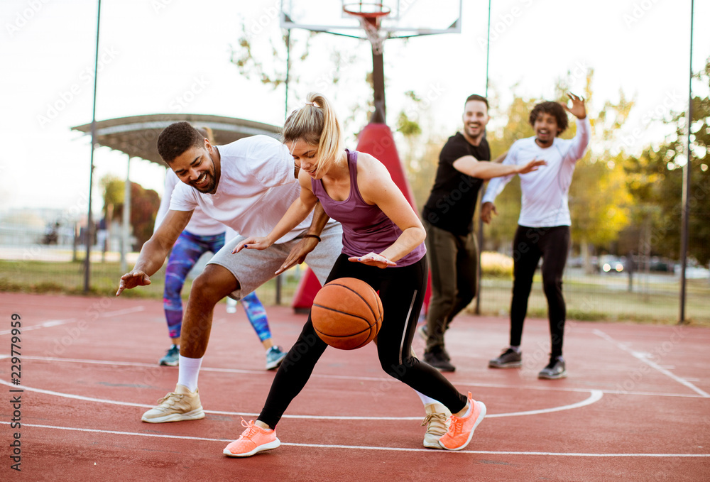 Group of multiracial young people   playing basketball outdoors