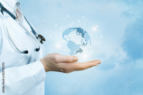 A female doctor with a stethoscope on her neck is holding a crystal, sparkling global map on her hand .