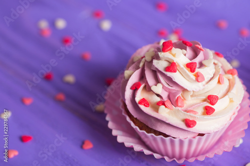 Closeup cupcake with creamy pink and white top decorated with little hearts on purple background