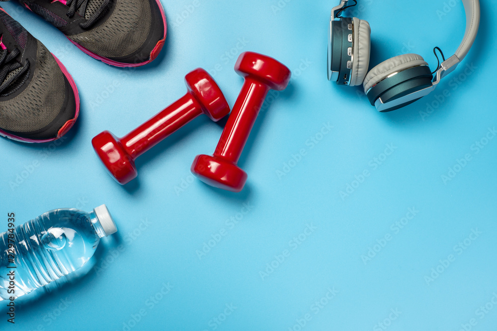 Fitness and health care concept of red dumbbells, athlete shoes, headphones and drinking water bottle on blue background, top view design with copy space