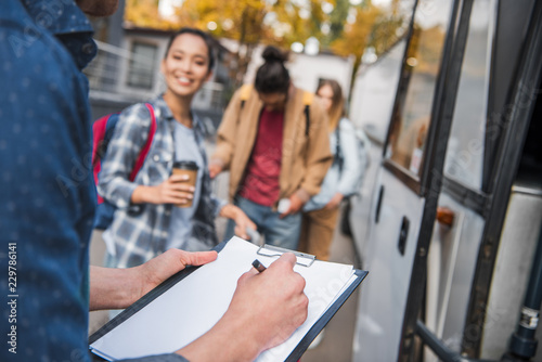 cropped image of travel bus controller writing in clipboard while tourists standing near bus at city street © LIGHTFIELD STUDIOS