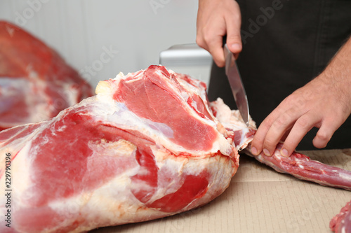 Butcher cutting fresh raw meat on counter in shop, closeup