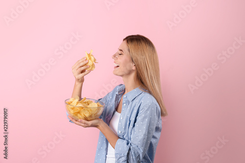 Woman eating potato chips on color background