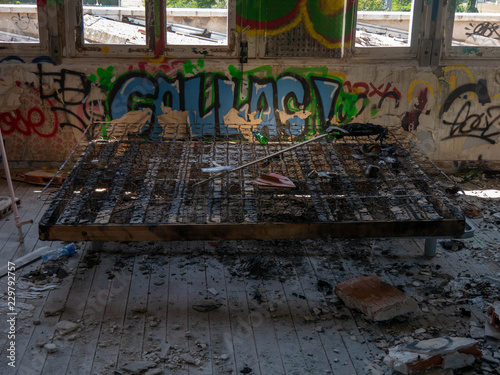 Burned bed in an old abandoned building or factory, completely destroyed and vandalized, painted with colourful graffiti street art