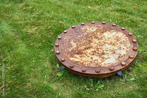 Rusty sewer manhole on green grass