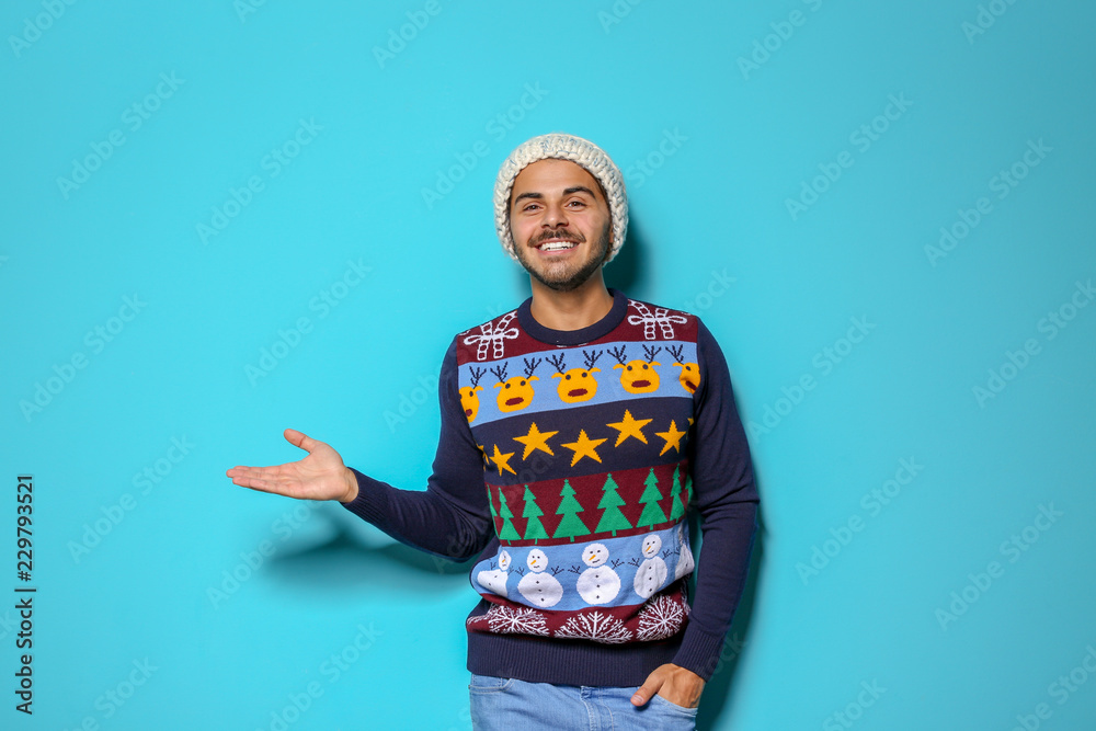 Young man in Christmas sweater and knitted hat on color background