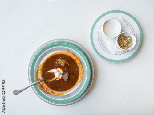 Meat soup kharcho with nuts and sour cream on a white table.