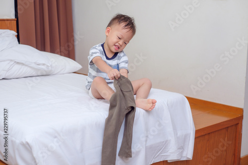 Schilderij op canvas Cute smiling little Asian 2 years old toddler boy child sitting in bed concentra