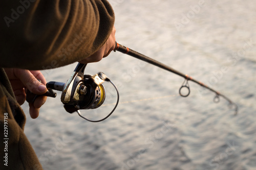Fishing rod, reel, fisherman fishing spinning on canal at sunset