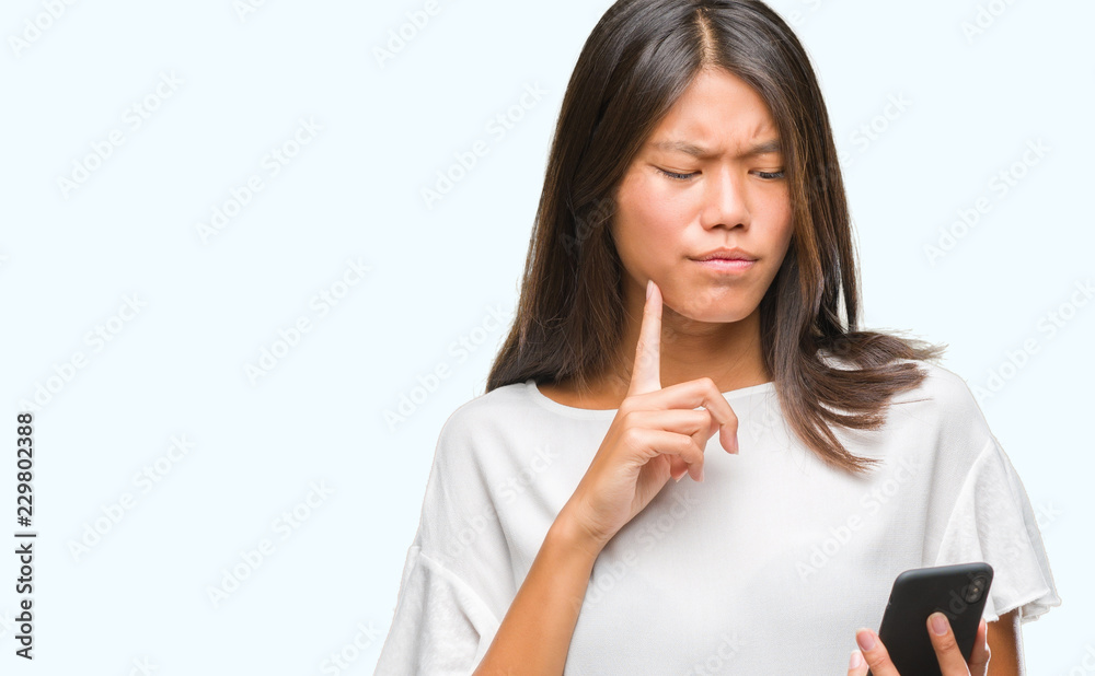Young asian woman texting using smartphone over isolated background serious face thinking about question, very confused idea Young asian woman texting using smartphone over isolated background serious face thinking about question, very confused idea