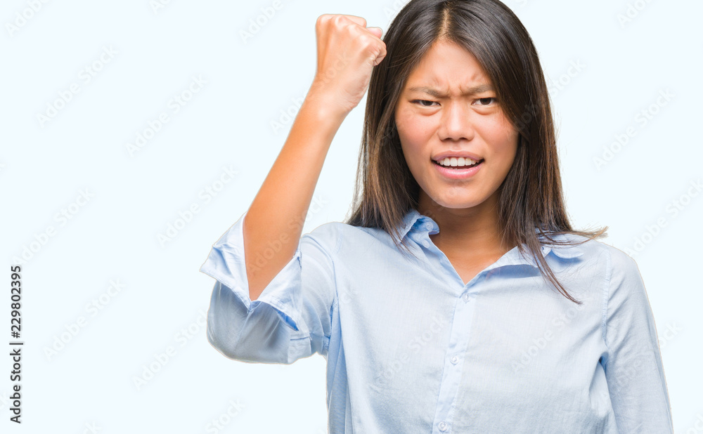 Young asian business woman over isolated background angry and mad raising fist frustrated and furious while shouting with anger. Rage and aggressive concept. Young asian business woman over isolated background angry and mad raising fist frustrated and furious while shouting with anger. Rage and aggressive concept.