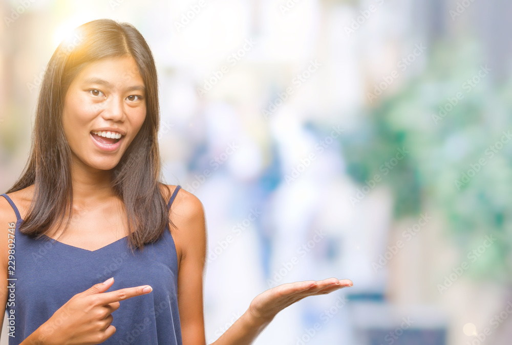 Young asian woman over isolated background amazed and smiling to the camera while presenting with hand and pointing with finger. Young asian woman over isolated background amazed and smiling to the camera while presenting with hand and pointing with finger.
