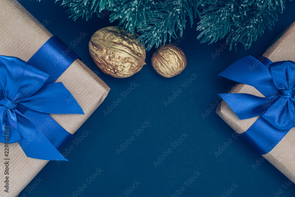Gifts in paper with blue ribbon and bow-knots with gold nuts and branches of spruce on a dark-blue background. - obrazy, fototapety, plakaty 